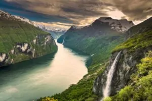 Vízesés zuhog a mélyzöld fjordba, körülötte havas hegycsúcsok